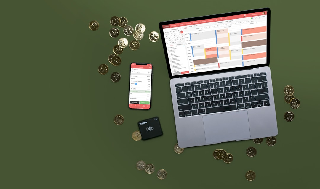 On a dark green background sits a laptop, phone, and credit card reader with gold coins scattered around it. the Laptop has a booking calendar displayed while the phone has a checkout screen.