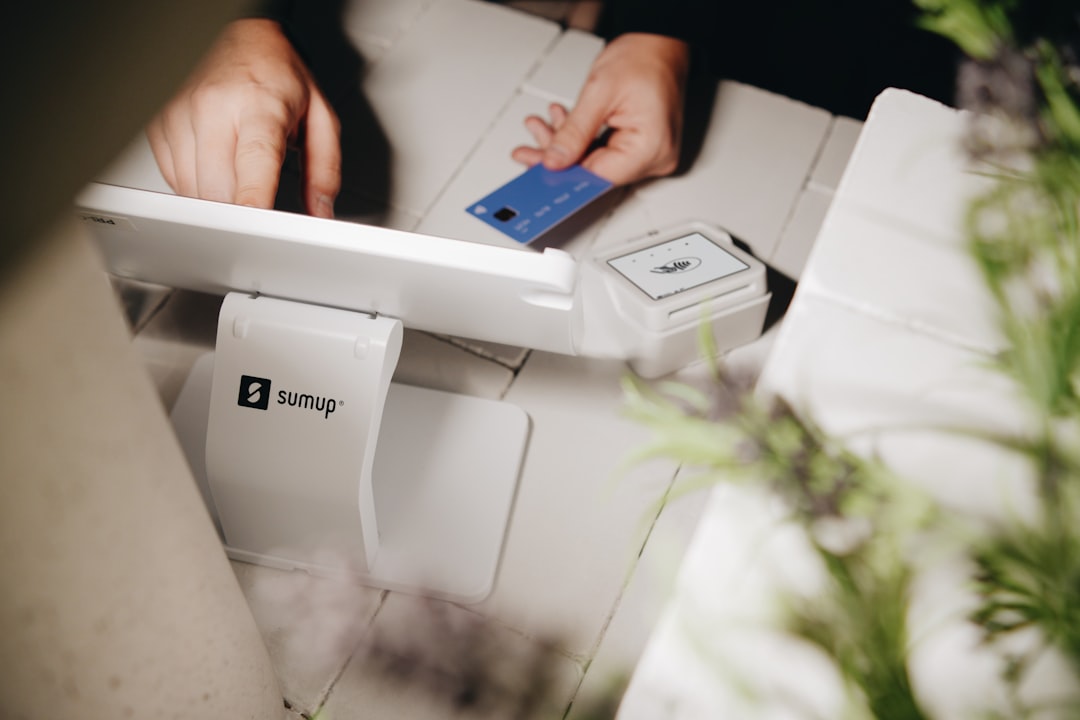 A customer making a contactless payment with a blue credit card on a SumUp reader at a small business. The modern point of sale setup with white tiles and soft lighting enhances the sleek and professional look of cashless transactions.